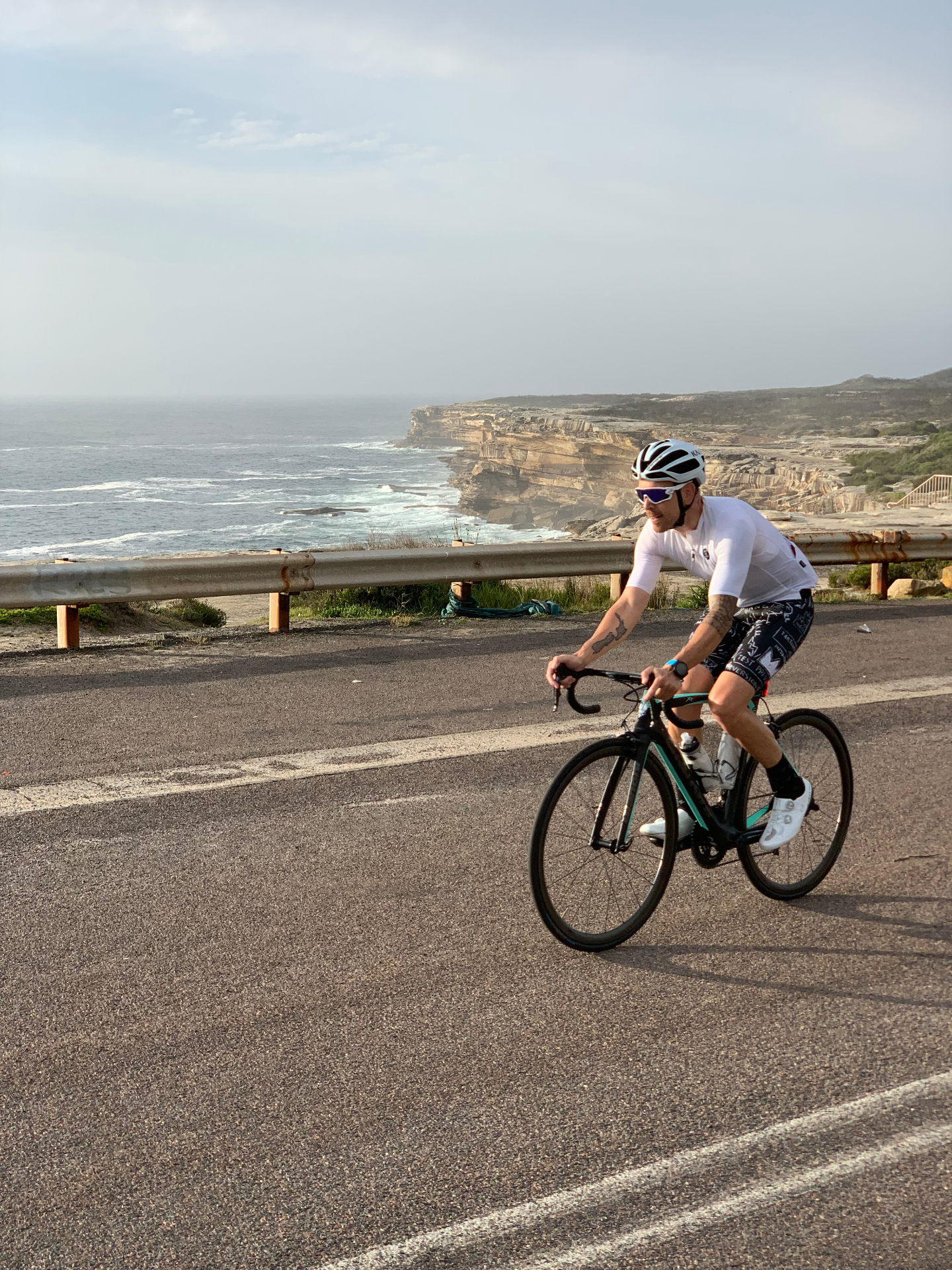 Phillipe cycling the coastal road, Sydney cliffs behind